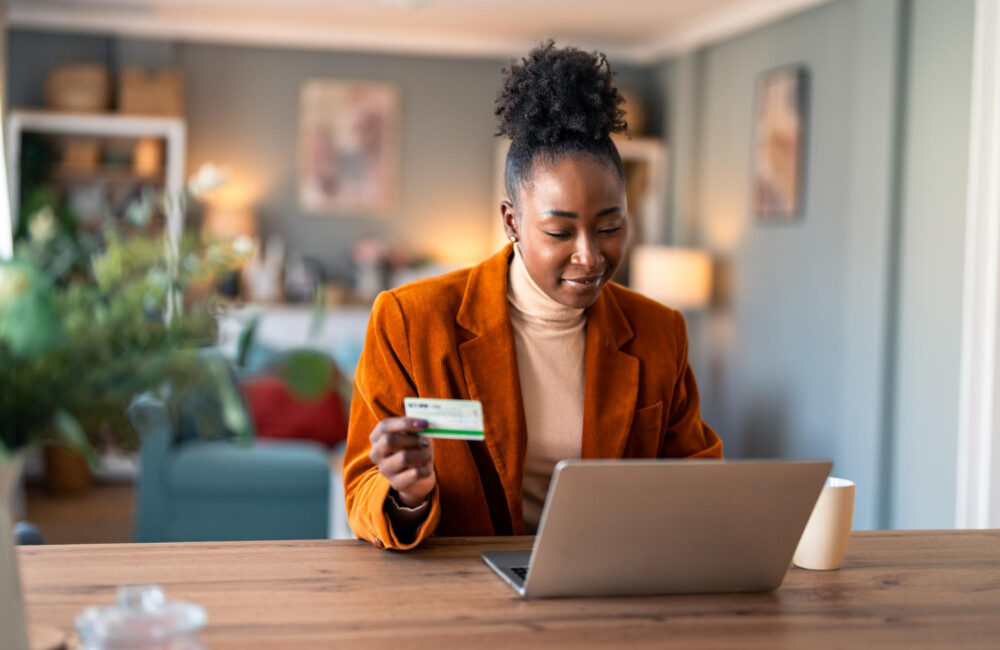 Woman shopping online on her laptop while holding a credit card at her desk.