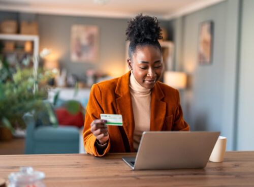 Woman shopping online on her laptop while holding a credit card at her desk.