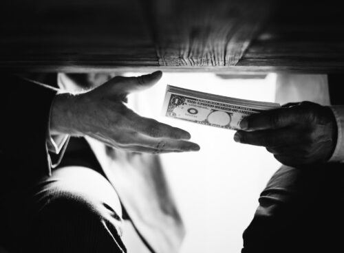 Hands exchanging cash under the table representing corruption, bribery, and financial crime risks linked to a politically exposed person (PEP)